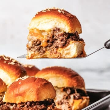 cheeseburger sliders on a baking sheet and a slider on a spatula