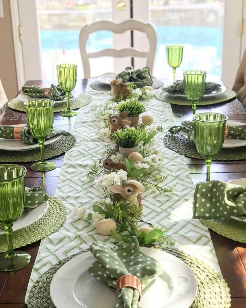 Easter Tablescape ideas, green and white lattice table runner, green placemats, white plates with green and white polka dot napkins. Green stemware. Bunny amd white flower scattered down the center of the table.