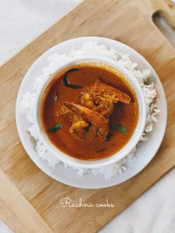 Mangalorean prawn curry in a bowl with rice on the side atop a cutting board.